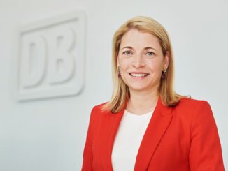 Evelyn Palla, bestuursvoorzitter van de Deutsche Bahn, in een rode blazer bij het DB-logo.