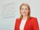 Evelyn Palla, bestuursvoorzitter van de Deutsche Bahn, in een rode blazer bij het DB-logo.