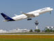 Een Lufthansa-vliegtuig stijgt op vanaf luchthaven München, met de verkeerstoren en terminal op de achtergrond.