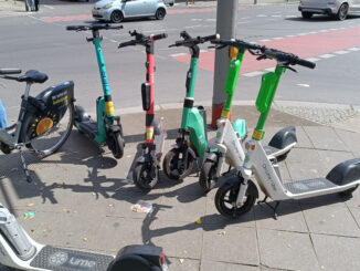 Een rij elektrische steps van deelbedrijven zoals Lime, Bolt en Tier geparkeerd op de stoep bij station Hermannstraße in Berlijn