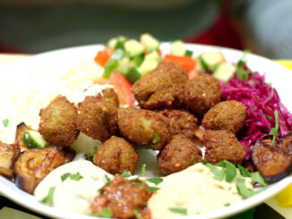 Bord met falafelballetjes, tahin, gegrilde aubergine en kleurrijke salade.