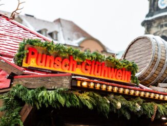 Een versierde kraam met het bord ‘Punsch-Glühwein’ op de Striezelmarkt in Dresden, met sneeuw en een houten wijnvat op het dak.