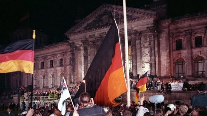 tagder Menigte viert de Duitse eenwording op 3 oktober 1990 voor het Rijksdaggebouw in Berlijn, met Duitse vlaggen en een grote zwart-rood-gouden vlag.