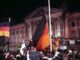 Menigte viert de Duitse eenwording op 3 oktober 1990 voor het Rijksdaggebouw in Berlijn, met Duitse vlaggen en een grote zwart-rood-gouden vlag.