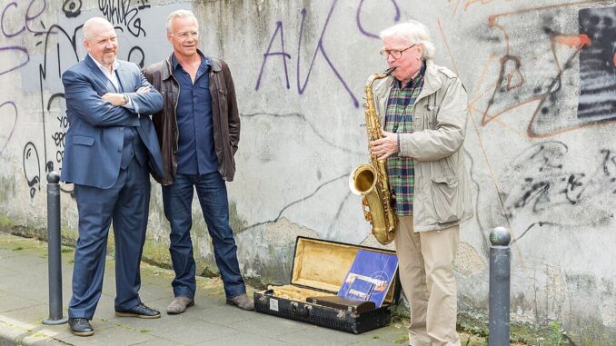 Saxofonist Klaus Doldinger speelt tijdens opnames van een Tatort-aflevering in Keulen, met naast hem acteurs Klaus J. Behrendt en Dietmar Bär.