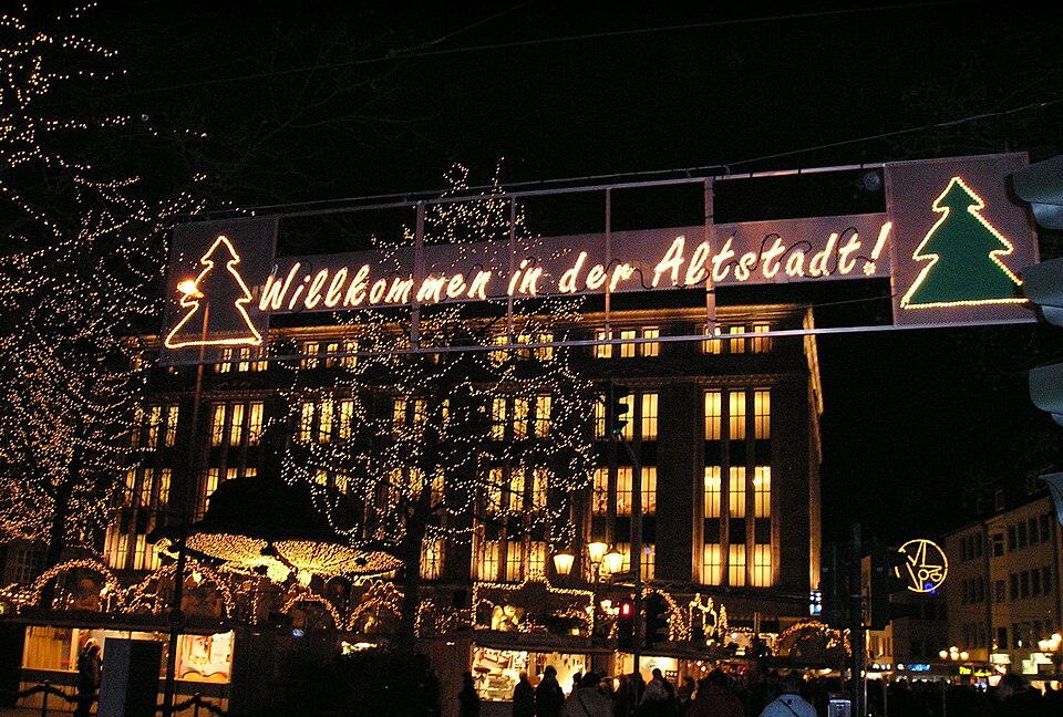 Verlichte kerstmarkt in de Altstadt van Düsseldorf met het bord “Willkommen in der Altstadt!”