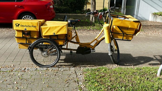 Een gele bezorgdriewieler van de Deutsche Post, geparkeerd langs de straat in München.