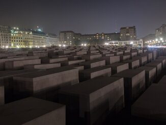 Holocaustmonument in Berlijn bij nacht met verlichte gebouwen op de achtergrond.