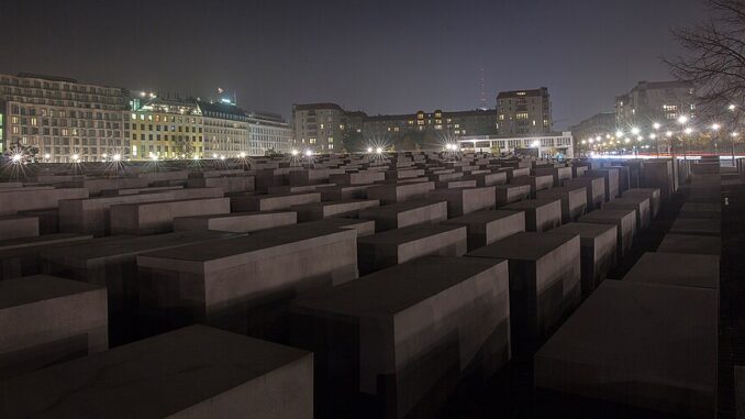 Holocaustmonument in Berlijn bij nacht met verlichte gebouwen op de achtergrond.