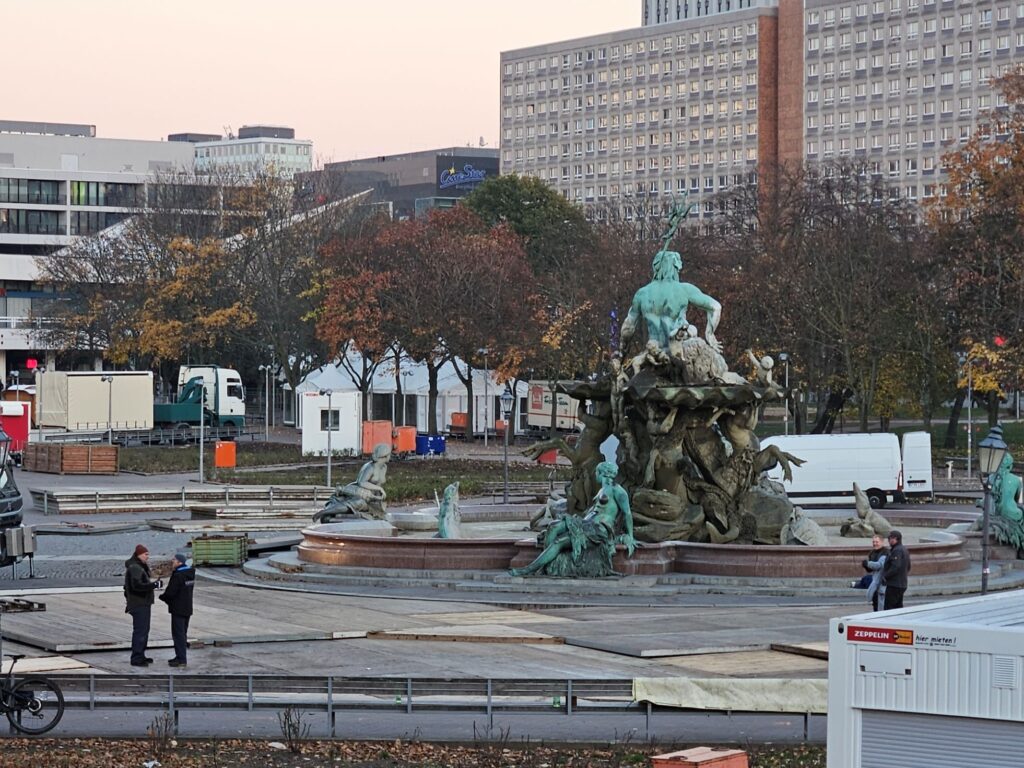 Opbouw van de kerstmarkt bij het Rote Rathaus in Berlijn: Neptunbrunnen met kraampjes en vrachtwagens op de achtergrond.
