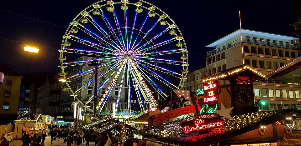 Reuzenrad en verlichte houten kraampjes op de kerstmarkt van Dortmund in de avond