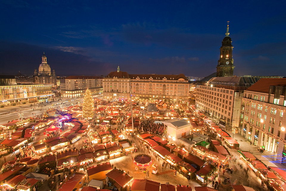 Striezelmarkt in Dresden bij avond, gezien van boven met verlichte kraampjes en de Frauenkirche op de achtergrond.