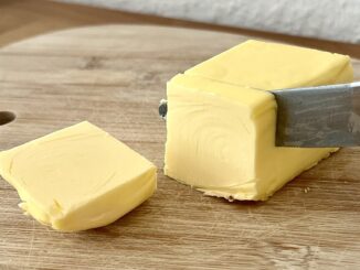 Een blok boter dat met een mes wordt aangesneden op een houten snijplank.