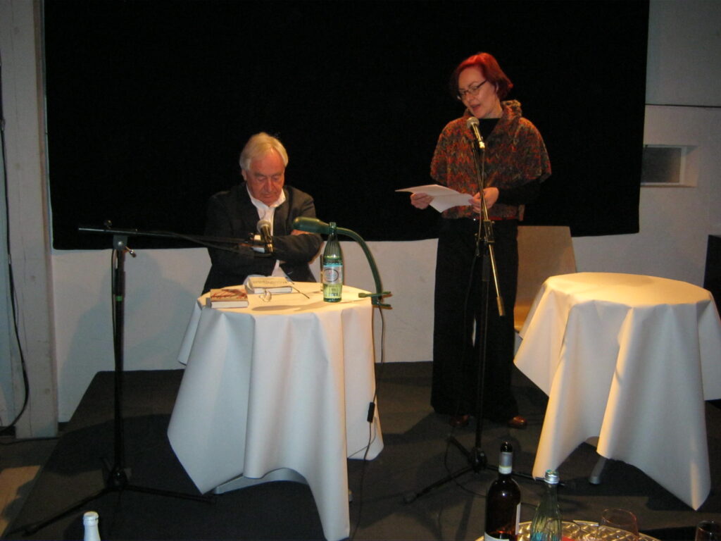 Cees Nooteboom zit aan tafel tijdens een literaire avond in Gschwend, terwijl een tekst wordt voorgelezen (2013)