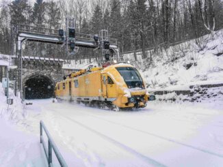 Geel instandhoudingsvoertuig van Deutsche Bahn rijdt door sneeuw bij tunnel tijdens winterweer