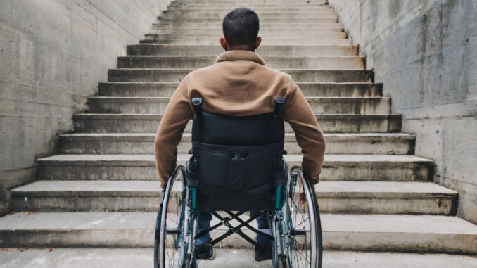 Man in rolstoel kijkt naar een trap zonder lift als symbool voor gebrekkige toegankelijkheid in Duitsland