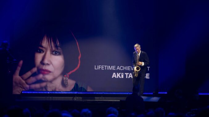 Groot portret van Aki Takase op scherm tijdens Deutscher Jazzpreis 2026 in Bremen, terwijl saxofonist Daniel Erdmann optreedt