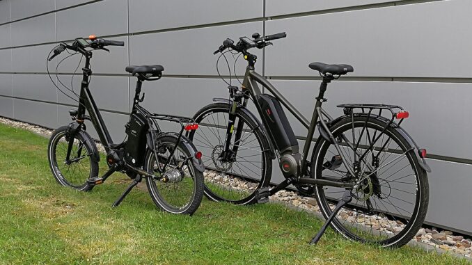 Twee e-bikes, een compacte en een trekkingfiets, geparkeerd naast een muur
