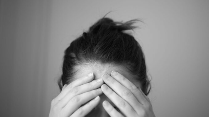Vrouw houdt haar hoofd vast als illustratie van uitputting en klachten bij Long Covid en ME/CVS
