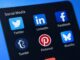 Smartphonescherm met social media apps zoals X (Twitter), LinkedIn, Facebook en Bluesky
