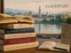Stapel boeken met op de achtergrond Klagenfurt als illustratie bij de Ingeborg Bachmannprijs 2026.