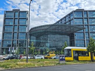 Vooraanzicht van het Berlijnse Hauptbahnhof met een gele tram op de voorgrond.