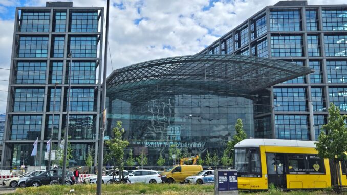 Vooraanzicht van het Berlijnse Hauptbahnhof met een gele tram op de voorgrond.