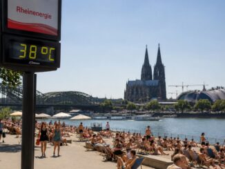 Mensen zoeken verkoeling aan de Rijn in Keulen terwijl een temperatuurdisplay 38 graden aangeeft tijdens een hittegolf.