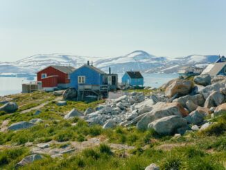 Het Groenlandse dorp Kullorsuaq met kleurrijke huizen, rotsen en besneeuwde bergen op de achtergrond.