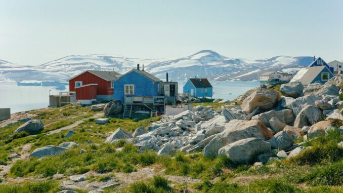 Het Groenlandse dorp Kullorsuaq met kleurrijke huizen, rotsen en besneeuwde bergen op de achtergrond.