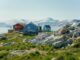 Het Groenlandse dorp Kullorsuaq met kleurrijke huizen, rotsen en besneeuwde bergen op de achtergrond.