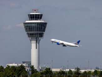 Verkeerstoren van München Airport met opstijgend vliegtuig tegen een dreigende lucht