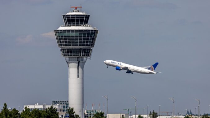 Verkeerstoren van München Airport met opstijgend vliegtuig tegen een dreigende lucht