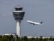 Verkeerstoren van München Airport met opstijgend vliegtuig tegen een dreigende lucht