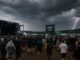 Festivalbezoekers op het Southside Festival onder donkere onweerswolken terwijl bliksem zichtbaar is aan de horizon.