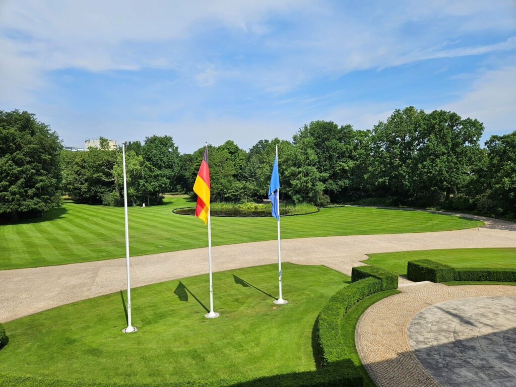 Uitzicht vanuit Schloss Bellevue op de achtertuin met vlaggenmasten, gazons en bomen in Berlijn.