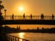 Mensen lopen tijdens een extreem warme zomeravond over een brug terwijl de lucht goudgeel kleurt door de hitte.