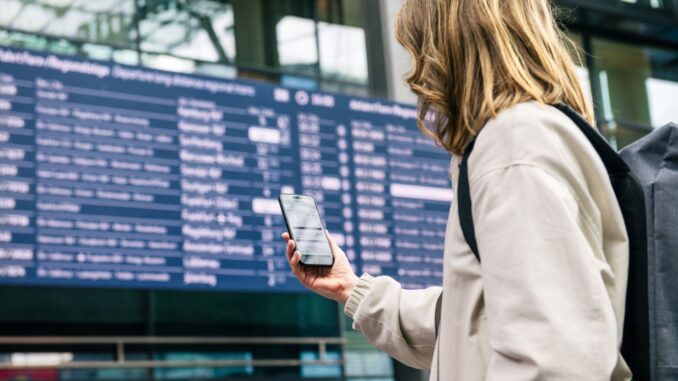 Reiziger bekijkt een smartphone voor het digitale vertrekbord in Berlin Hauptbahnhof.