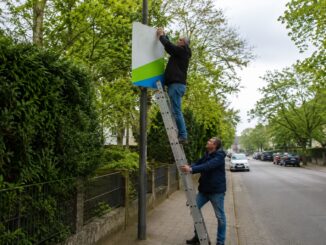 AI-illustratie van twee mannen die een verkiezingsposter aan een lantaarnpaal ophangen in een woonstraat in aanloop naar de deelstaatverkiezingen in Saksen-Anhalt.