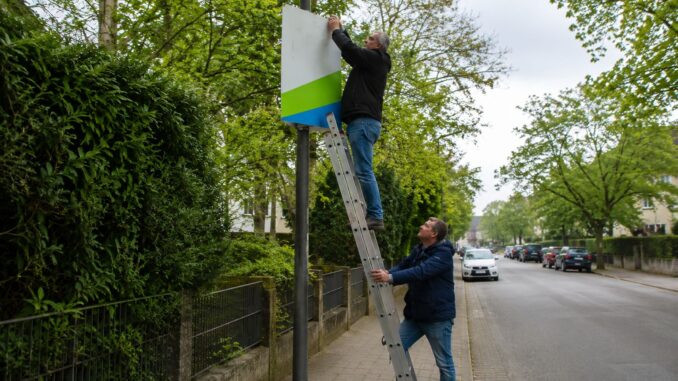 AI-illustratie van twee mannen die een verkiezingsposter aan een lantaarnpaal ophangen in een woonstraat in aanloop naar de deelstaatverkiezingen in Saksen-Anhalt.